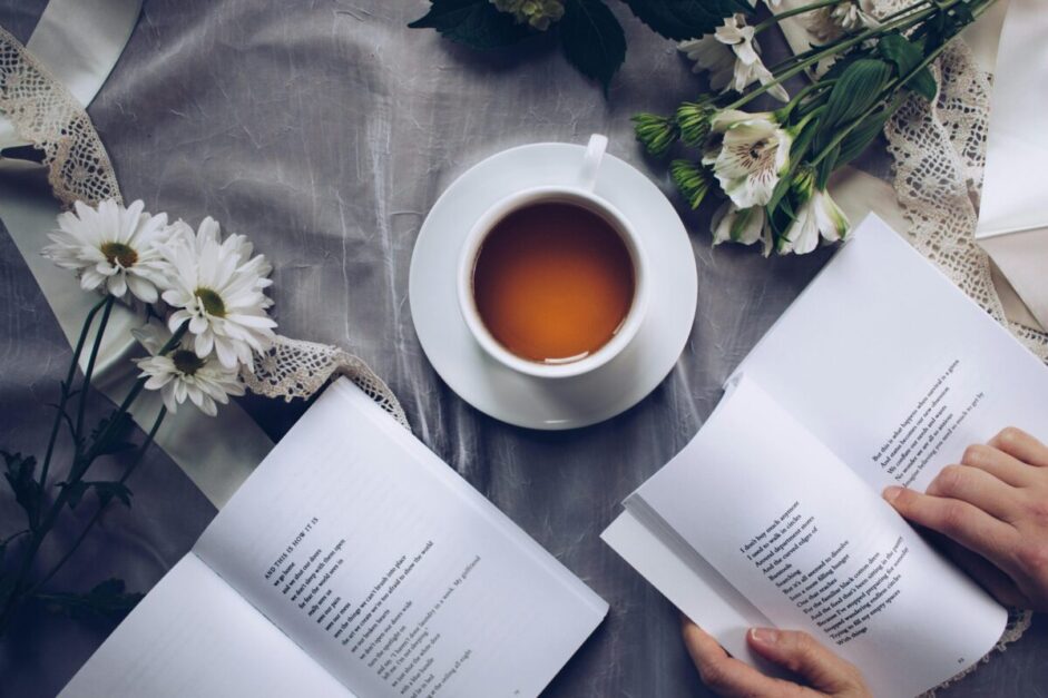 Inviting cozy reading setup with tea, poetry books, and fresh flowers on a table.